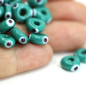 Puede incluir: Cuentas de vidrio azul turquesa con un diseño de ojo blanco y negro. Las cuentas tienen un agujero en el centro para enhebrar.
