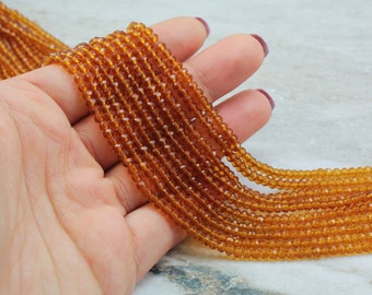 May include: A strand of amber-colored faceted glass beads. The beads are small and round, and they are strung on a clear thread. The beads are arranged in a loose, flowing pattern.