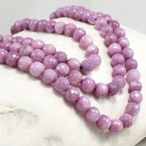 Peut inclure: Un collier de perles violet clair à facettes. Les perles sont rondes et de forme légèrement irrégulière. Les perles sont enfilées ensemble. Les perles sont d'une couleur violet clair et douce. Chaque perle mesure environ 0,8 cm de diamètre.