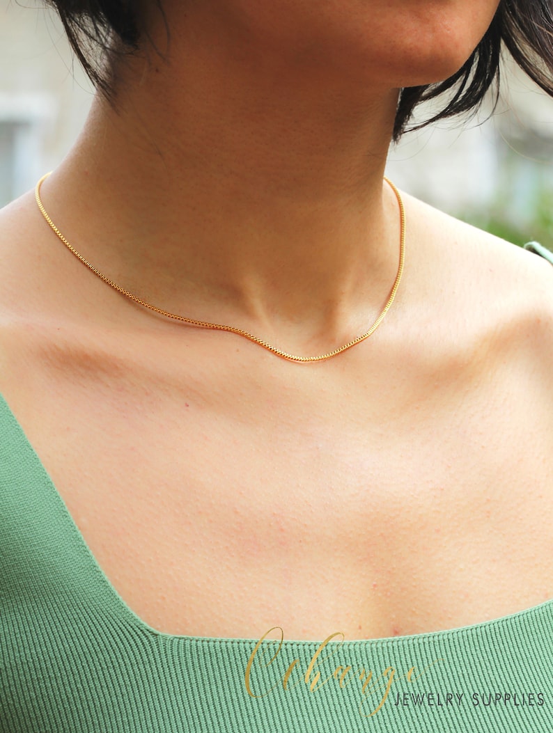 May include: A delicate gold chain necklace worn by a model in a green top.