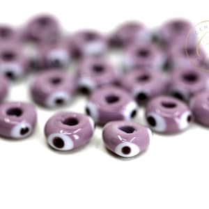 Puede incluir: Un conjunto de cuentas de vidrio de color lavanda con forma de rosquilla y un diseño de ojo blanco y marrón. Estas cuentas son ideales para la fabricación de joyas y proyectos de artesanía. Las cuentas miden aproximadamente 1,3 cm de diámetro.