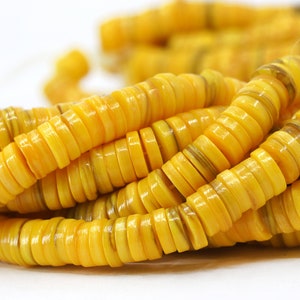 May include: Close-up of strands of yellow, disc-shaped beads. The beads have a glossy finish and are strung together, creating a necklace or bracelet. The beads are a warm yellow color with some brown marbling.