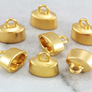 May include: Six gold-toned metal oval-shaped pendant caps with a loop at the top. The caps are designed to be used as end caps for necklaces or bracelets.