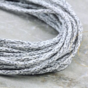 May include: A close-up of a strand of white and gray ceramic beads. The beads are small and have a checkered pattern. The beads are arranged in a coil shape.
