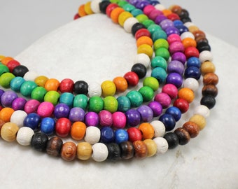 May include: A strand of colorful wooden beads, each bead is a different color, including red, orange, yellow, green, blue, purple, and white. The beads are arranged in a circular pattern, creating a rainbow effect.
