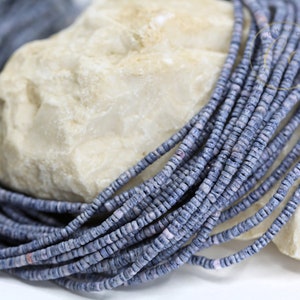 May include: A strand of light blue and white shell beads. The beads are small and round, and they are strung together on a thin thread. The beads are arranged in a loose pile, and they are resting on a white surface.