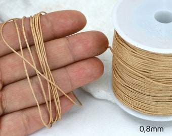 May include: A spool of 0.8mm thick, beige elastic cord. The cord is wound tightly around the spool and is shown in a close-up view.