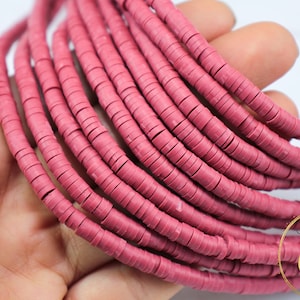 May include: A strand of pink clay beads, each bead is a flat disc with a hole in the center. The beads are stacked on top of each other, creating a layered effect.