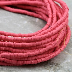 May include: A close-up of a spool of pink polymer clay beads. The beads are small and round, and they are arranged in a tight coil.