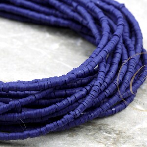 May include: A close-up of a strand of dark blue round polymer clay beads. The beads are small and uniform in size and shape. The beads are arranged in a coil.