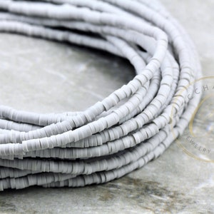 May include: A close-up of a spool of light gray ceramic beads. The beads are small and round, and they are arranged in a coil.