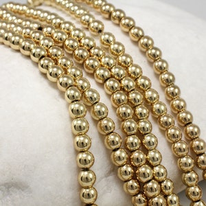 May include: A strand of gold-colored round beads. The beads are smooth and shiny.