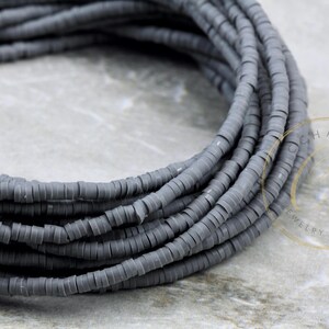 May include: A close-up of a strand of gray ceramic beads. The beads are round and have a matte finish. The beads are arranged in a coil shape.