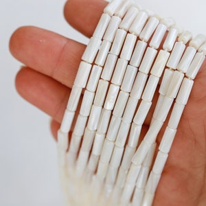 Pu&ograve; includere: Una collana di perline bianche di conchiglia, ogni perlina ha la forma di un tubo rettangolare.