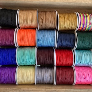 May include: Assortment of spools of colourful waxed cotton cord, arranged in rows. The cords are in various colours, including pink, red, blue, green, yellow, and brown.