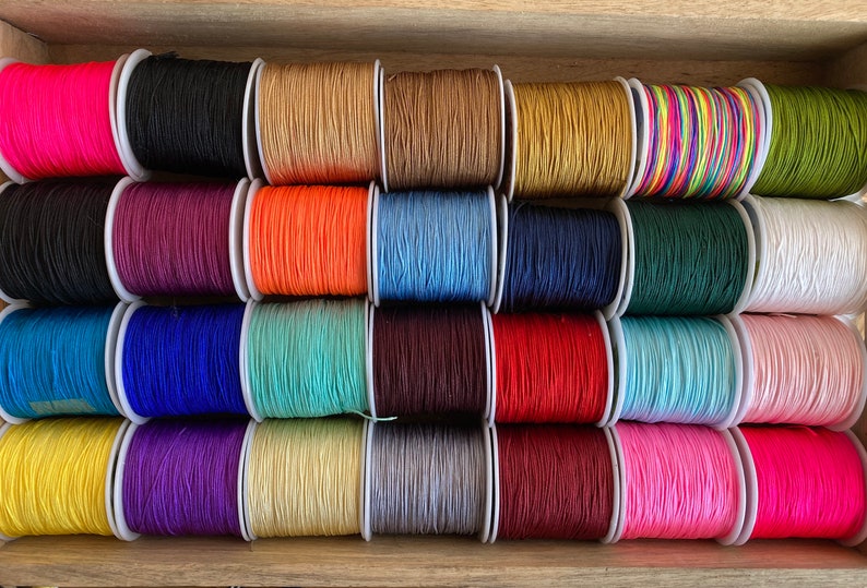 May include: Assortment of spools of colourful waxed cotton cord, arranged in rows. The cords are in various colours, including pink, red, blue, green, yellow, and brown.