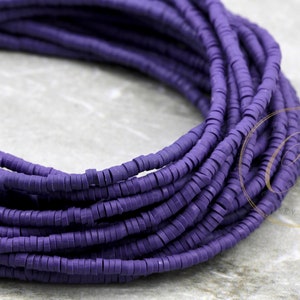 May include: Close-up of a bundle of dark purple, flat, disc-shaped beads. The beads are stacked in a spiral, revealing their uniform shape and color. These beads are likely used for jewelry making or other craft projects.