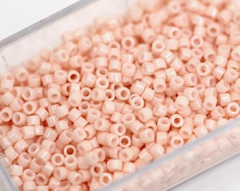 May include: A clear plastic container filled with numerous small, cylindrical, light peach-colored beads. The beads are uniform in size and shape, with a hole running through the center of each. Ideal for jewelry making and crafts.