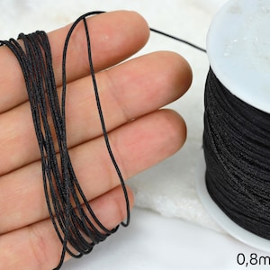 Könnte beinhalten: Eine Spule mit schwarzem elastischem Kordel, 0,8 mm dick, für die Schmuckherstellung oder Bastelarbeiten.