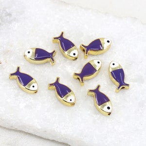 May include: Eight purple and gold fish charms with white eyes. The charms are on a white surface.