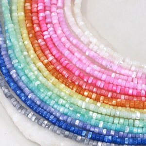 Könnte beinhalten: Eine Regenbogen-Auswahl an irisierenden quadratischen Perlen, jede Perle hat eine andere Farbe und einen dezenten Schimmer.