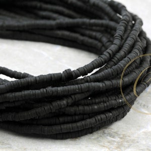 May include: A close-up of a strand of black rubber beads. The beads are small and round, and they are arranged in a tight coil.