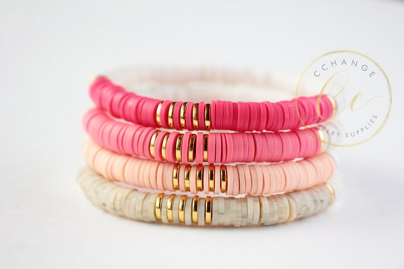 May include: Four stacked bracelets with pink, peach, and white ceramic beads and gold spacers. The bracelets are layered in a gradient from pink to white.