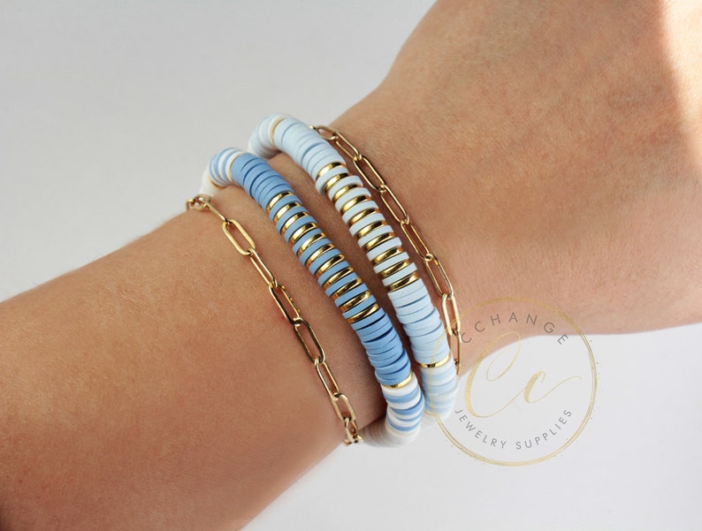 May include: A stack of three bracelets with blue and white ceramic beads and a gold chain link bracelet. The bracelets are on a person's wrist.