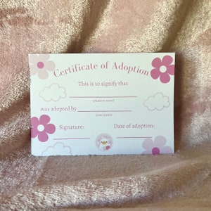 May include: A white certificate of adoption with pink flowers and clouds. The text reads "Certificate of Adoption" and "This is to signify that (plushies name) was adopted by (your name)". There are blank lines for the signature and date of adoption.