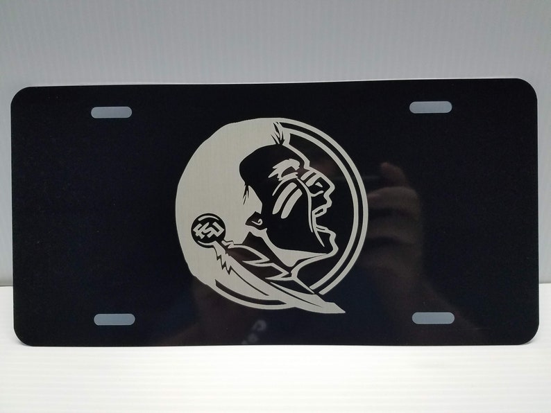 May include: Black metal license plate with a white Seminole Indian head logo. The logo is a profile of a Native American man with a feather and the letters FSU.