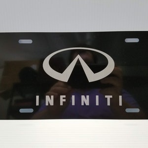May include: Black metal license plate with a silver Infiniti logo and the word "INFINITI" in silver lettering.