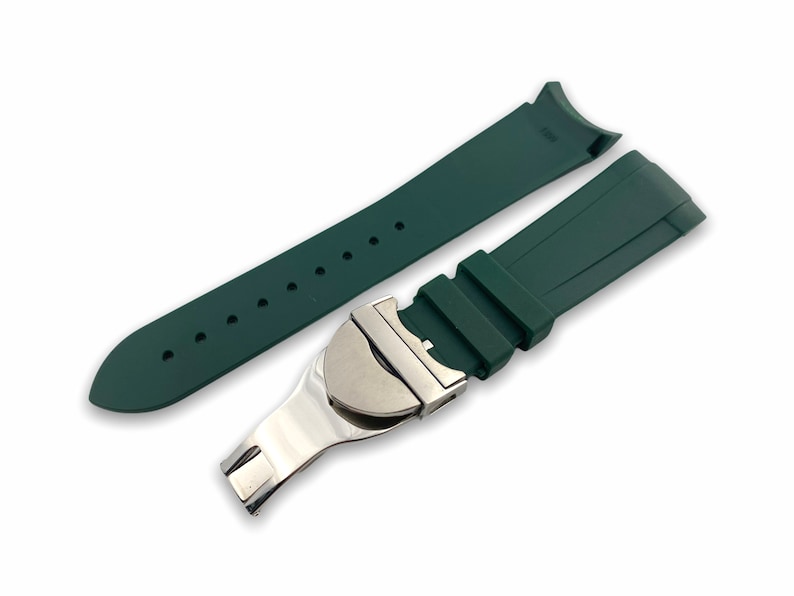 May include: A dark green rubber watch strap with a silver buckle. The strap is designed for a watch with a lug width of 20mm.