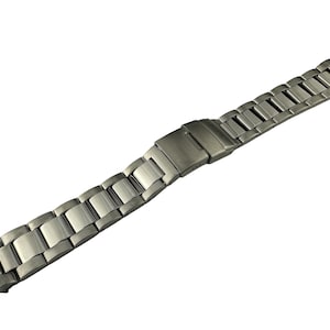 May include: A silver-toned metal watch band with a brushed finish. The band is composed of rectangular links connected by a folding clasp. The watch band is shown against a white background.
