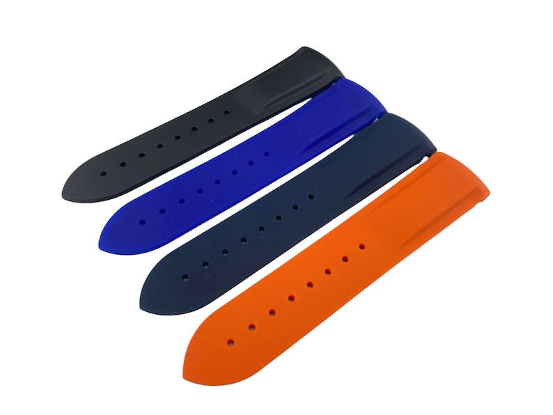 Może przedstawiać: Cztery paski do zegarka w r&oacute;żnych kolorach: czarny, niebieski, ciemnoniebieski i pomarańczowy. Paski są wykonane z gumy i mają fakturowaną powierzchnię.