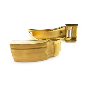 K&ouml;nnte beinhalten: Ein goldfarbener Uhrenarmbandverschluss mit geb&uuml;rsteter Oberfl&auml;che. Der Verschluss ist ge&ouml;ffnet und bereit, an ein Uhrenarmband befestigt zu werden.