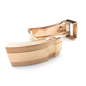 K&ouml;nnte beinhalten: Eine goldfarbene Uhrenarmband-Schlie&szlig;e mit polierter Oberfl&auml;che. Die Schlie&szlig;e verf&uuml;gt &uuml;ber einen sicheren Verschlussmechanismus und ein glattes, abgerundetes Design.