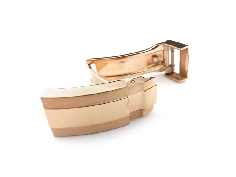 K&ouml;nnte beinhalten: Eine goldfarbene Uhrenarmband-Schlie&szlig;e mit polierter Oberfl&auml;che. Die Schlie&szlig;e verf&uuml;gt &uuml;ber einen sicheren Verschlussmechanismus und ein glattes, abgerundetes Design.