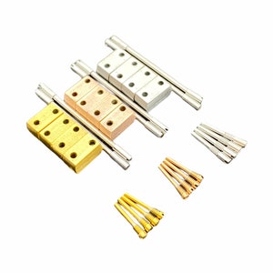 May include: Three sets of metal bridge pins for a guitar, each set in a different colour: gold, copper, and silver. The pins are arranged in rows on a white background.