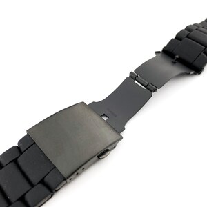 May include: Black watch strap with a metal buckle. The strap is made from a rubber-like material and has a matt finish.