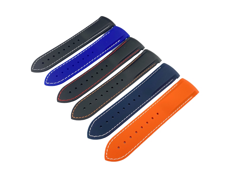 May include: Five different colored watch bands with white stitching. The bands are made of rubber and have a textured surface. The bands are arranged in a row from top to bottom, with the black band at the top and the orange band at the bottom.