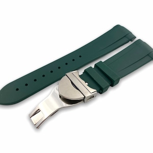 Puede incluir: Una correa de reloj de silicona verde oscuro con una hebilla plateada. La correa tiene una superficie texturizada y está diseñada para un reloj con una anchura de lengüeta de 22 mm.