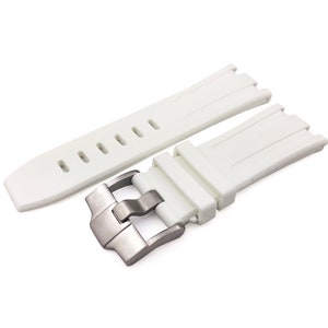 May include: A white watch strap with a silver-coloured buckle. The strap is made of a flexible material and has a series of holes for adjustment. The buckle has a brushed metal finish.