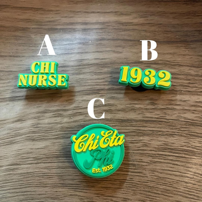 Puede incluir: Tres dijes de zapatos verdes y amarillos. Uno dice "CHI NURSE", otro dice "1932" y el tercero dice "Chi Eta Phi Est. 1932". Los dijes est&aacute;n hechos de un material gomoso.