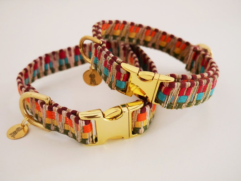 May include: Two colorful dog collars with gold-tone hardware. The collars are woven with red, orange, yellow, green, blue, and brown threads. The collars have gold-tone buckles and D-rings.