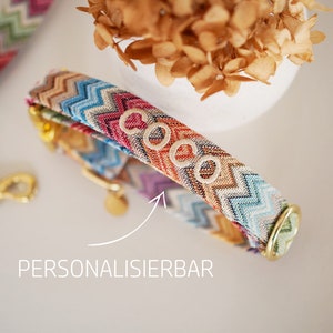 May include: A colorful dog collar with a chevron pattern and the name "Coco" embroidered on it. The collar is made of fabric and has a gold metal buckle.