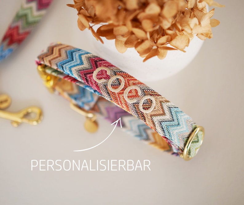 May include: A colorful dog collar with a chevron pattern and the name "Coco" embroidered on it. The collar is made of fabric and has a gold metal buckle.