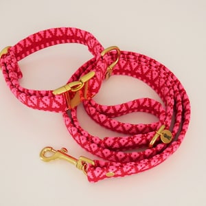 May include: A pink dog collar and leash set with a gold buckle and a gold tag that says "Woof".