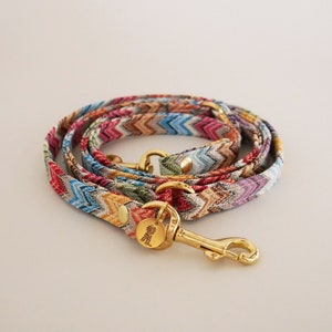 May include: A colorful dog leash with a chevron pattern and a gold metal clasp. The leash is made of woven fabric and has a  "Small" tag.