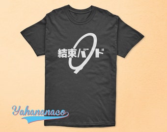 May include: A dark gray t-shirt featuring a white graphic design with Japanese characters and a stylized oval shape. The text reads "結束バンド". The shirt is a casual wear item.