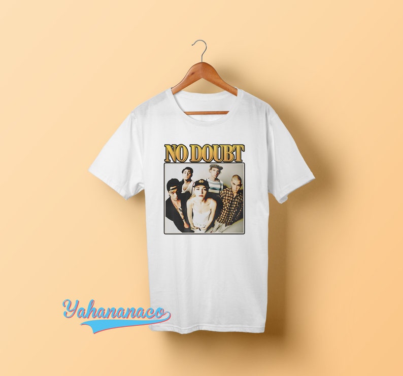 May include: White t-shirt with a vintage-style graphic of the band No Doubt. The graphic features a photo of the band members, including Gwen Stefani, Tony Kanal, Adrian Young, Tom Dumont, and  the band's name in gold letters.
